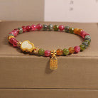 Multicolored beaded bracelet with gold charms on a beige surface