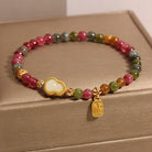 Multicolored beaded bracelet with gold charm on a beige surface